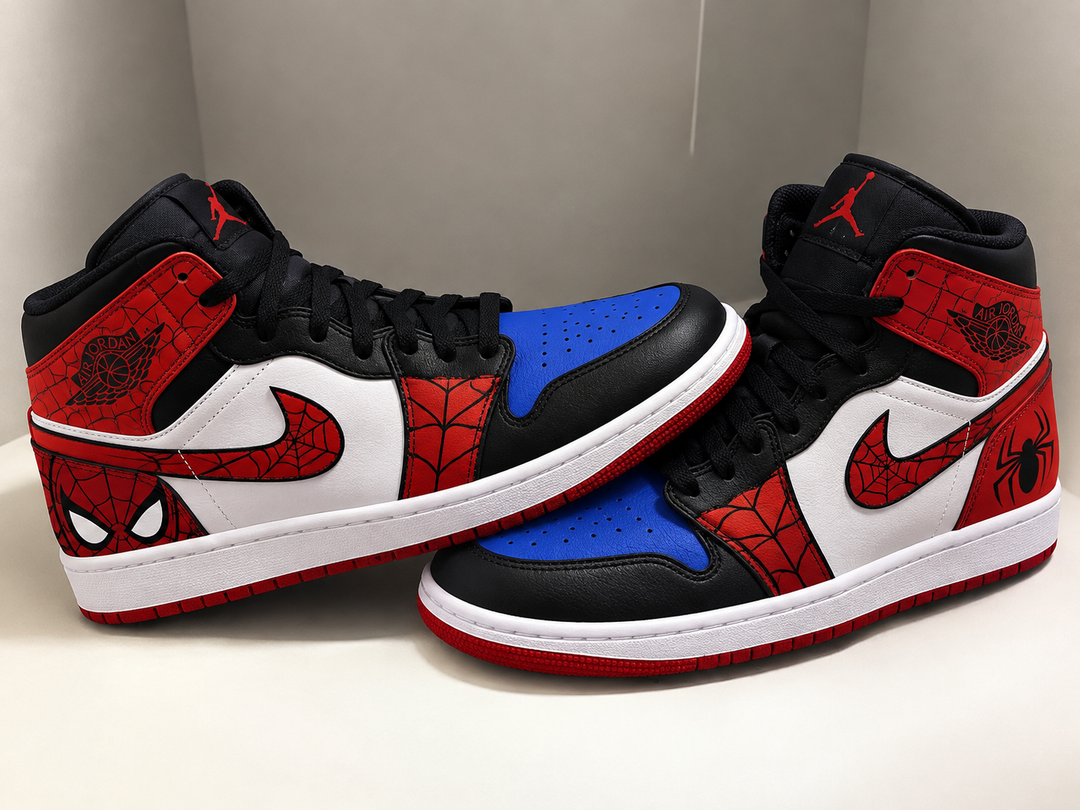 A pair of high-top sneakers styled like Air Jordan 1 Mid sneakers with Spider-Man theme panels, featuring red, black, and white colors with a blue toe cap accent.