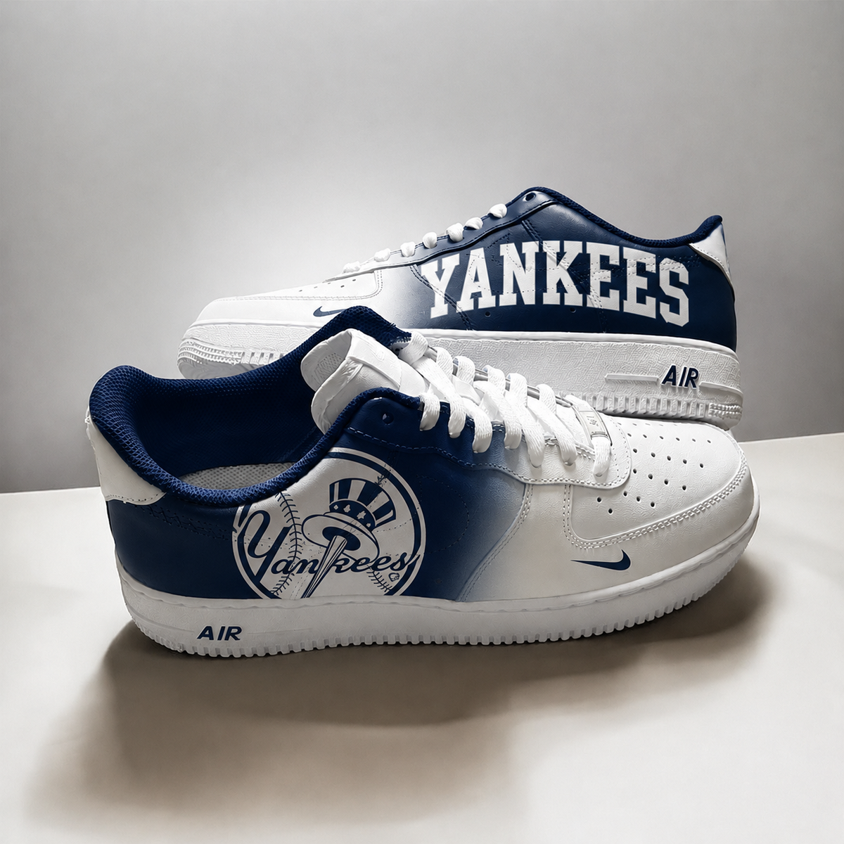 A pair of Nike Air Force 1 Low sneakers in a white and navy blue gradient design, featuring the New York Yankees logo and 'YANKEES' text on the side